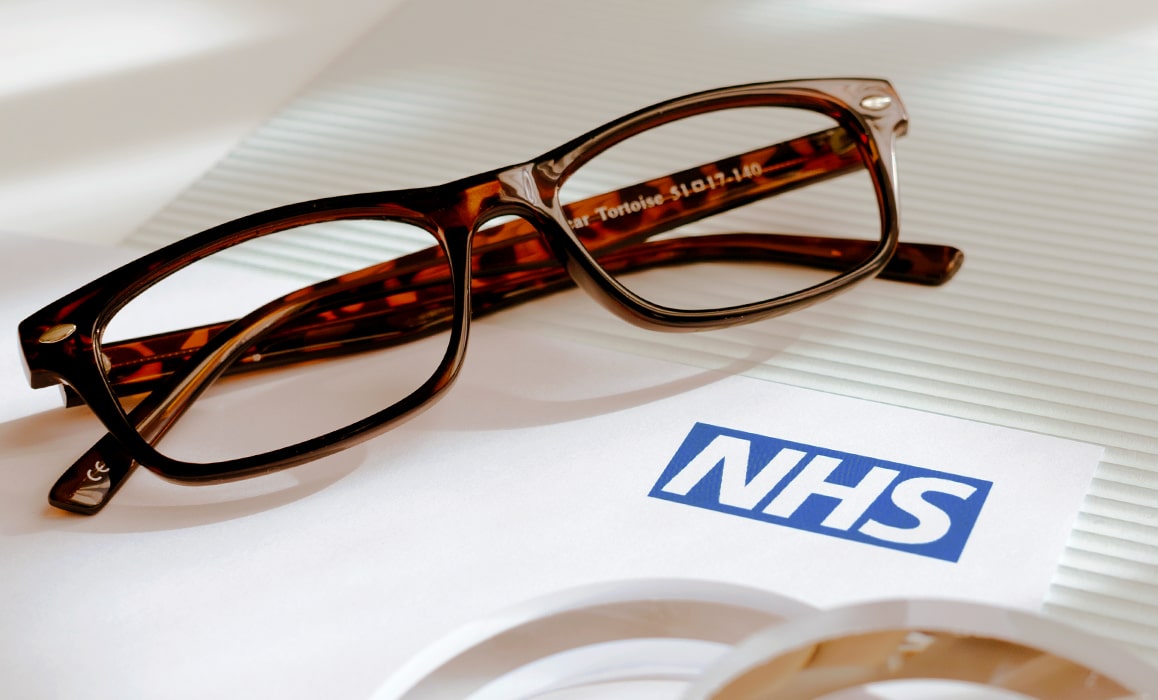 Glasses frames and lenses lying on a piece of paper with the NHS logo