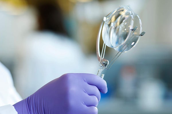 A gloved hand holding up two glasses lenses with a tool