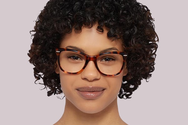 Woman with full head of curly black hair wearing tortoiseshell wayfarer frames