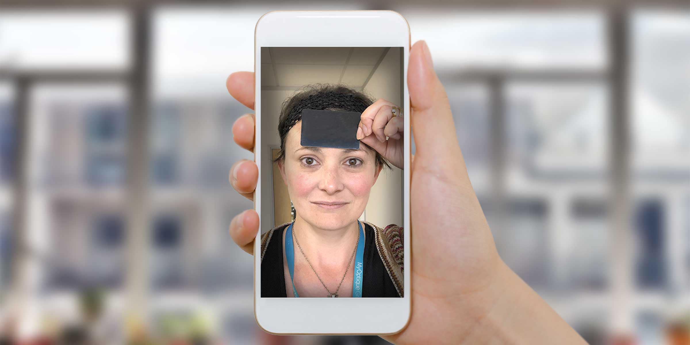 Portrait of a woman holding a blacked out credit or store card up to her forehead while looking straight ahead