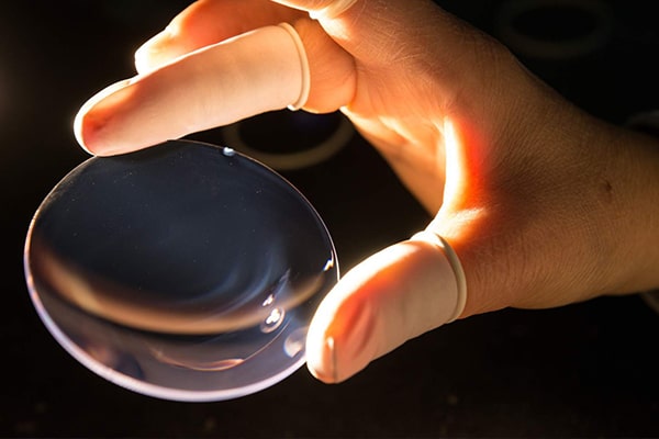 Close-up of a hand holding a glasses lens under a light