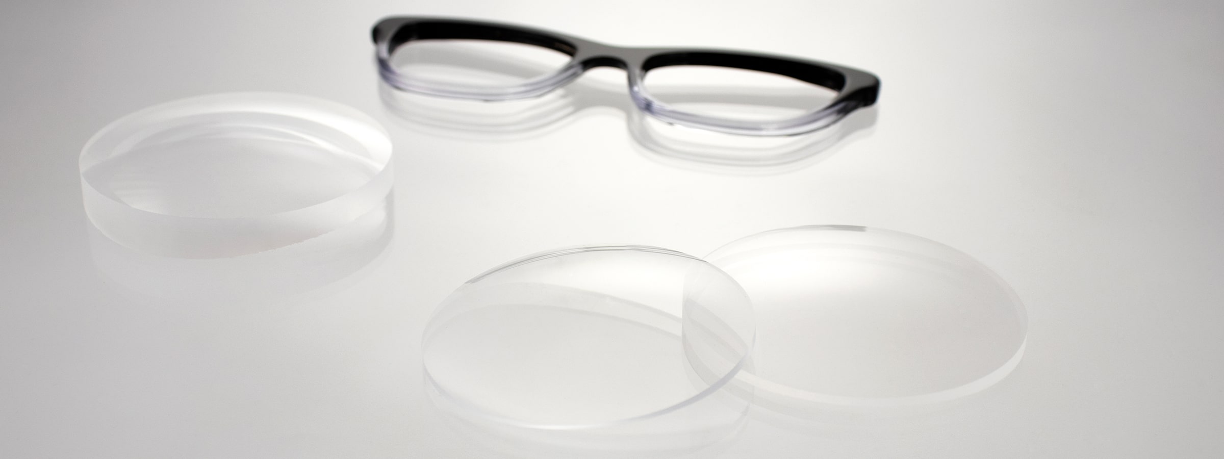 The front of a black-and-white glasses frame lying next to three uncut lenses on a table