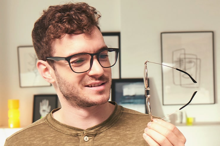 A young man wearing black glasses in his home inspects a metal frame