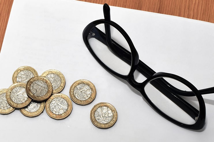 A black pair of glasses lying on a table next to nine pound coins