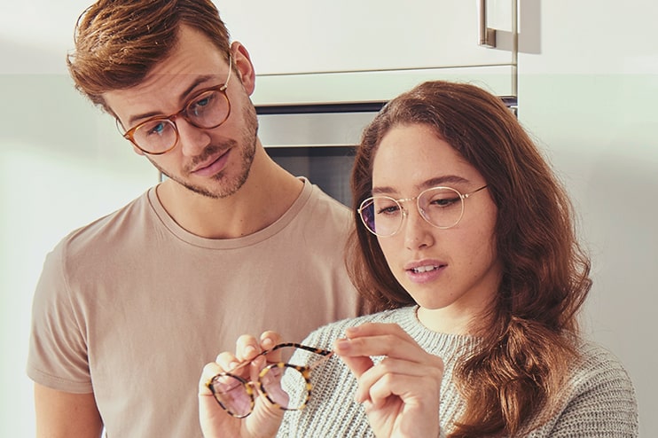 A young man and woman looking at a pair of glasses in their home