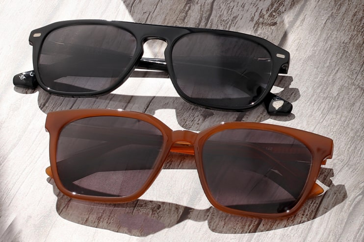 A black and a brown pair of sunglasses lying on a wooden table