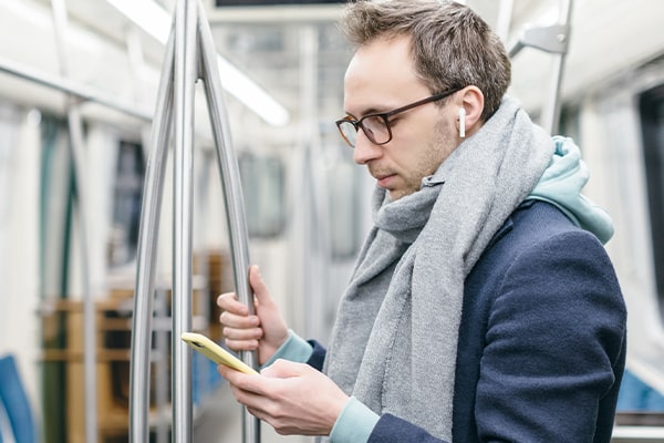 Man wearing glasses looking at his phone on the tube