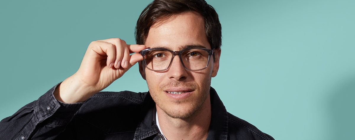 Man holding side of his glasses deciding if the glasses suit him