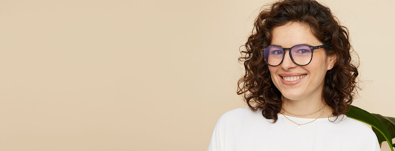A smiling woman with curly hair wearing glasses with blue light lenses