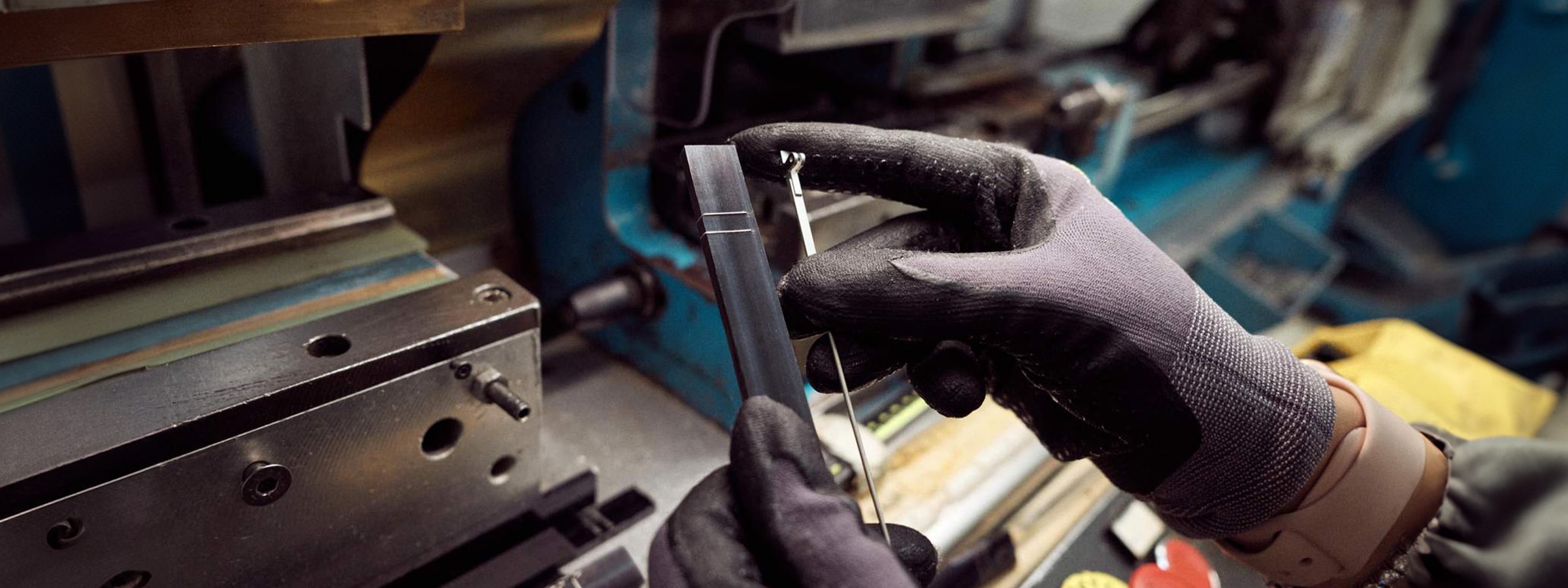 A pair of gloved hands working on some glasses parts next to heavy machinery