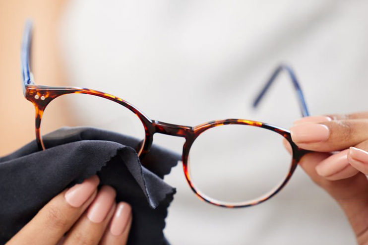 Close-up of a woman's hands holding up a pair of glasses and cleaning it with a lens cloth