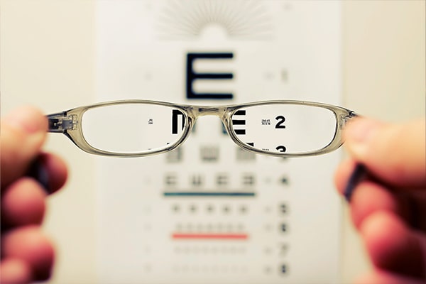 Pair of small glasses being held up to an eye test letter board
