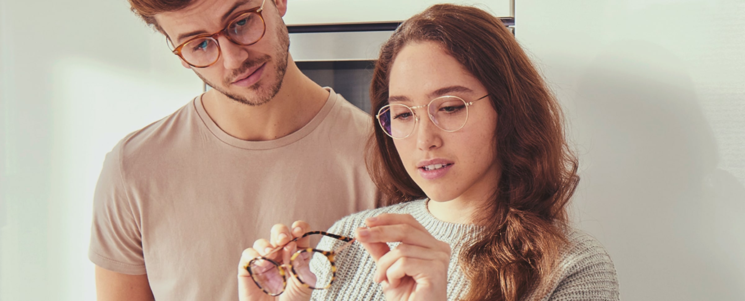 A young man and woman looking at a pair of glasses in their home