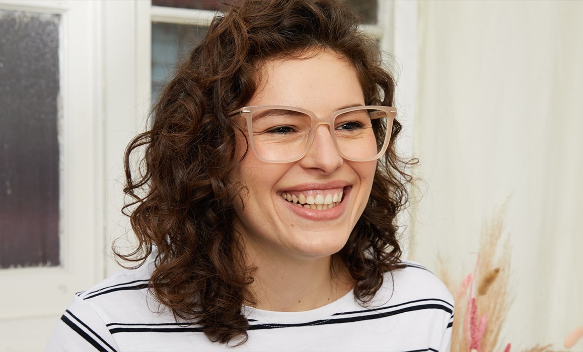 Smiling woman with brown, curly hair wearing large, nude-coloured cat-eye glasses
